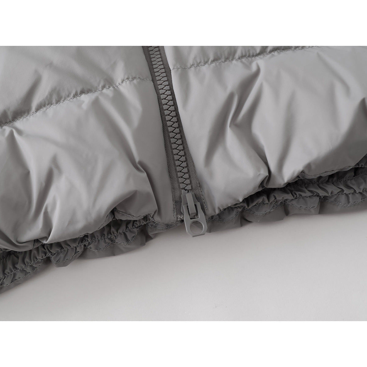 Close-up of the light gray jacket's lower front zipper and gathered hem.