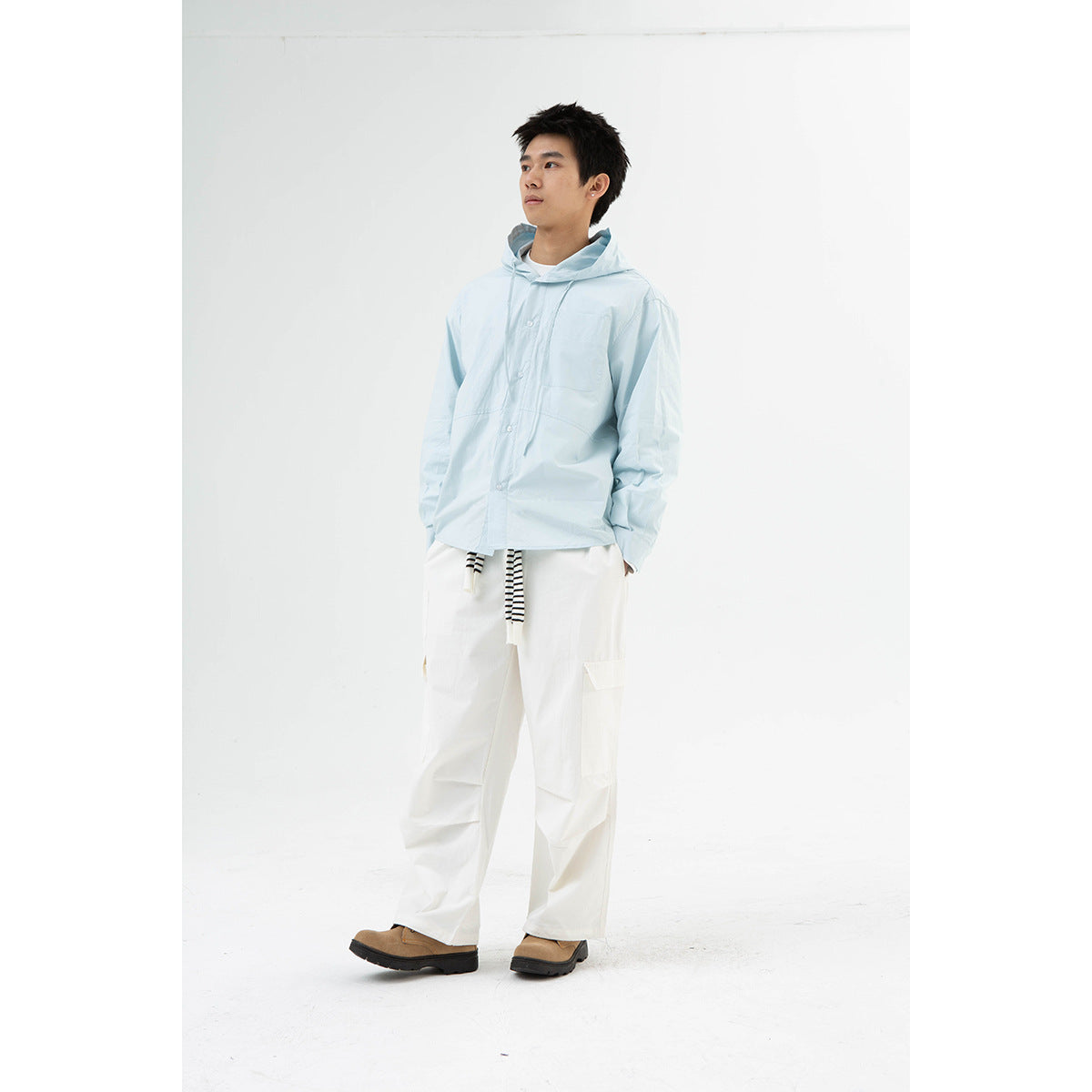 Model wearing a pale blue hooded button-front shirt with a chest pocket and white cargo pants.