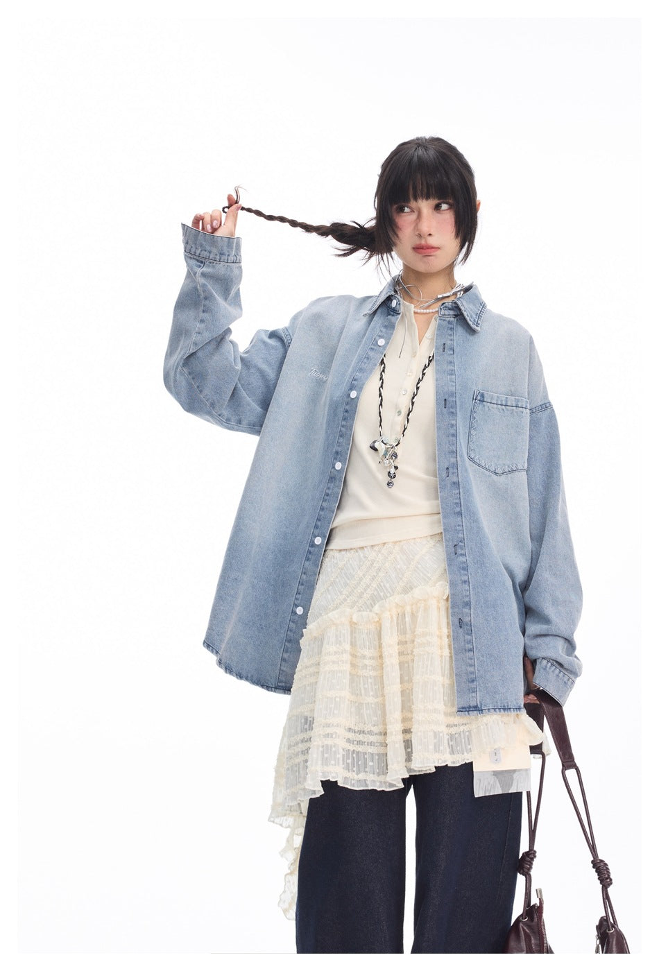 Model wearing an oversized light blue denim button-front shirt with a chest pocket, layered over a cream top and dark