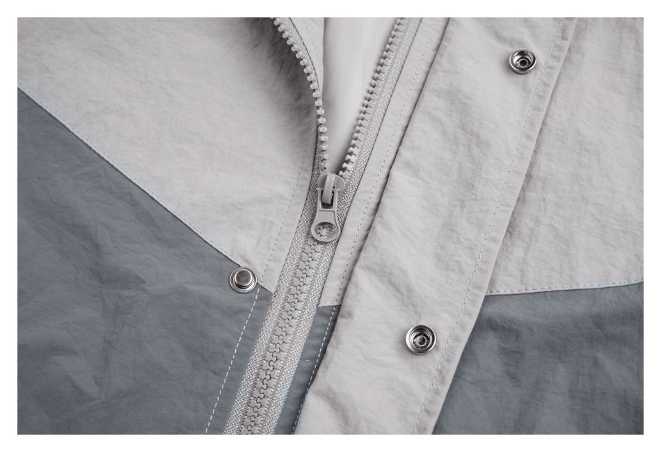 Close-up of the jacket’s gray zipper and metal snap fasteners on a two-tone front panel.