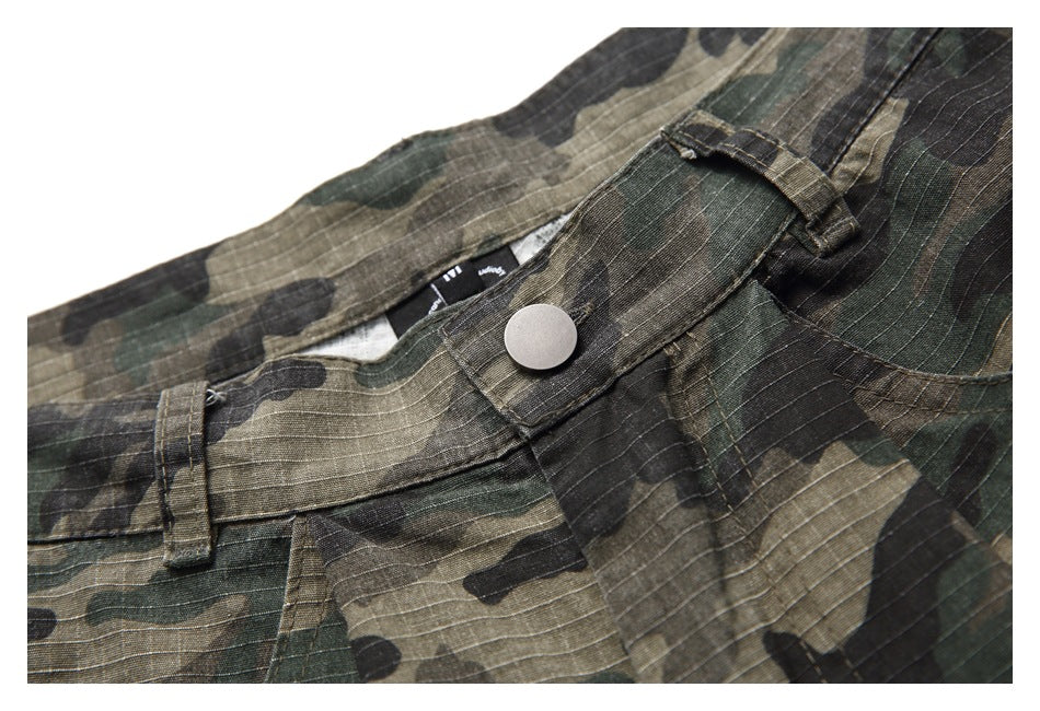 Close-up of camouflage trousers at the front waistband, with a silver button, belt loop and fly seam.