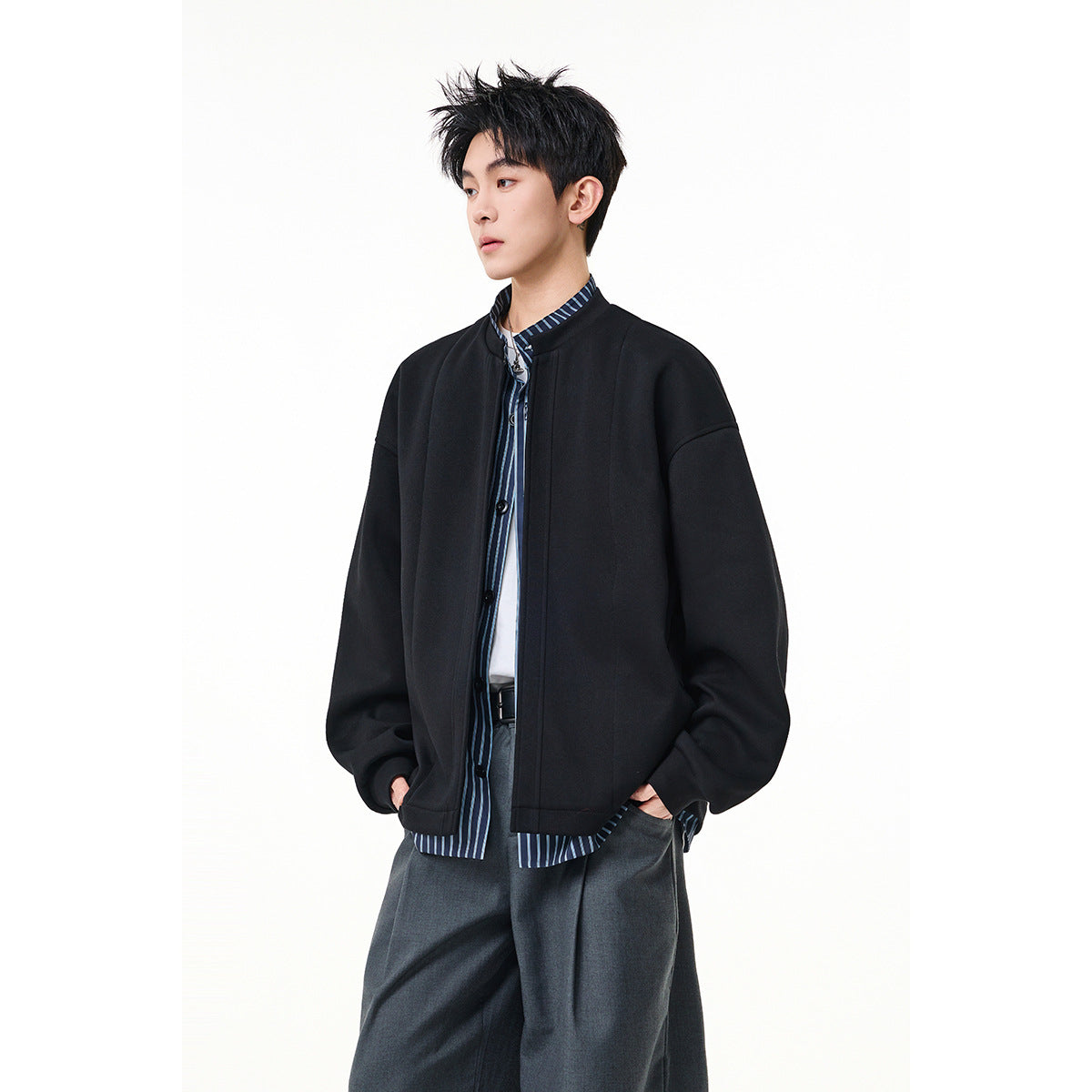 Model wearing a black oversized jacket over a blue striped shirt, with dark gray trousers.