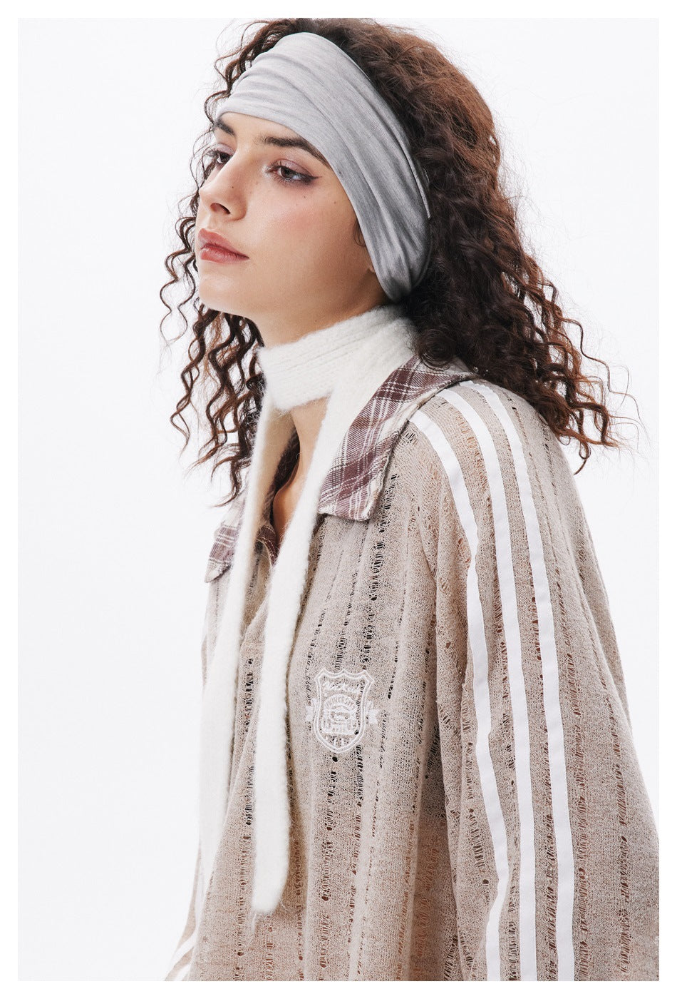 Close side view of a model wearing a beige open-knit pullover with white sleeve stripes and a plaid collar.