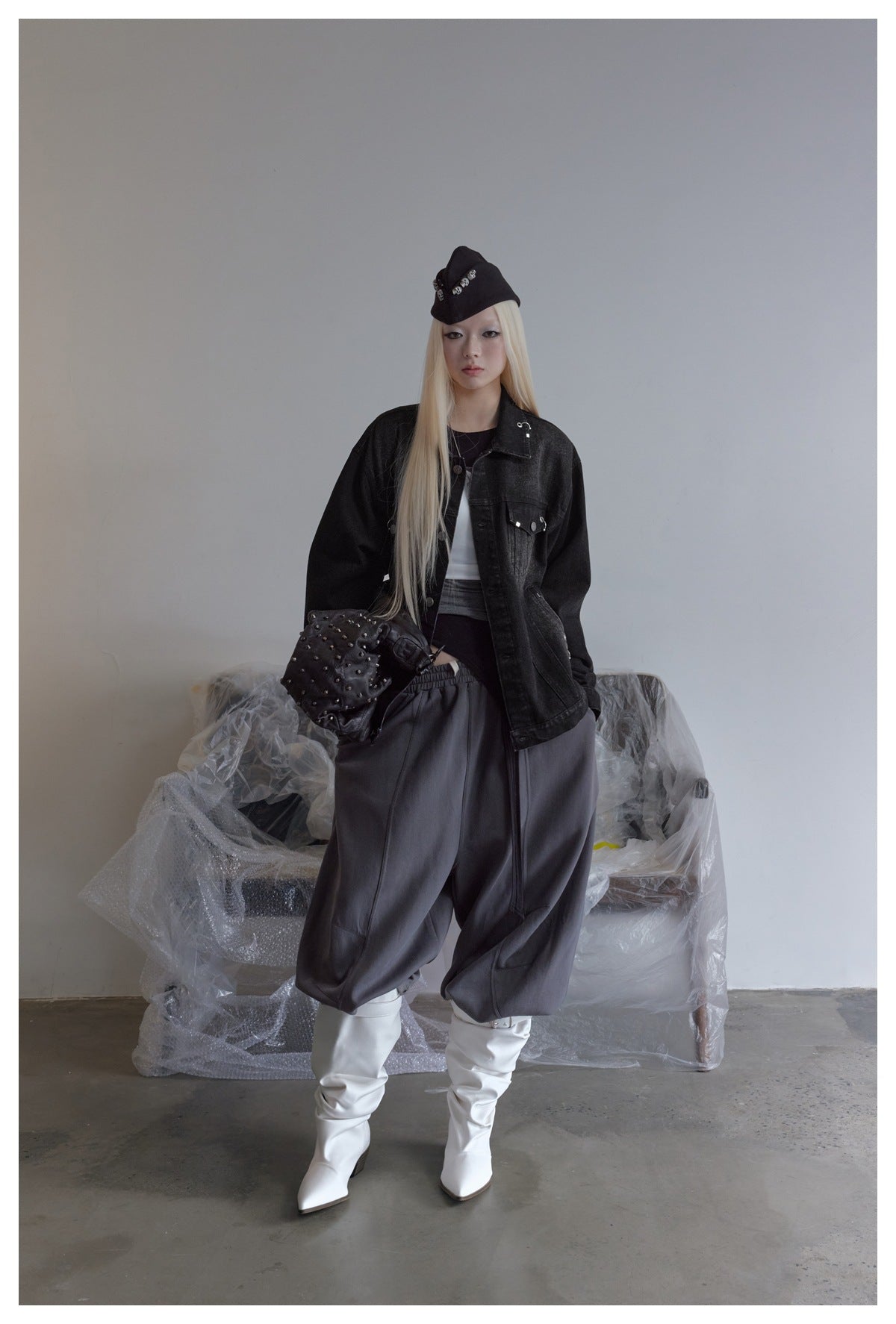 Model wearing black washed denim jacket with hardware details, white top, gray baggy pants and white boots