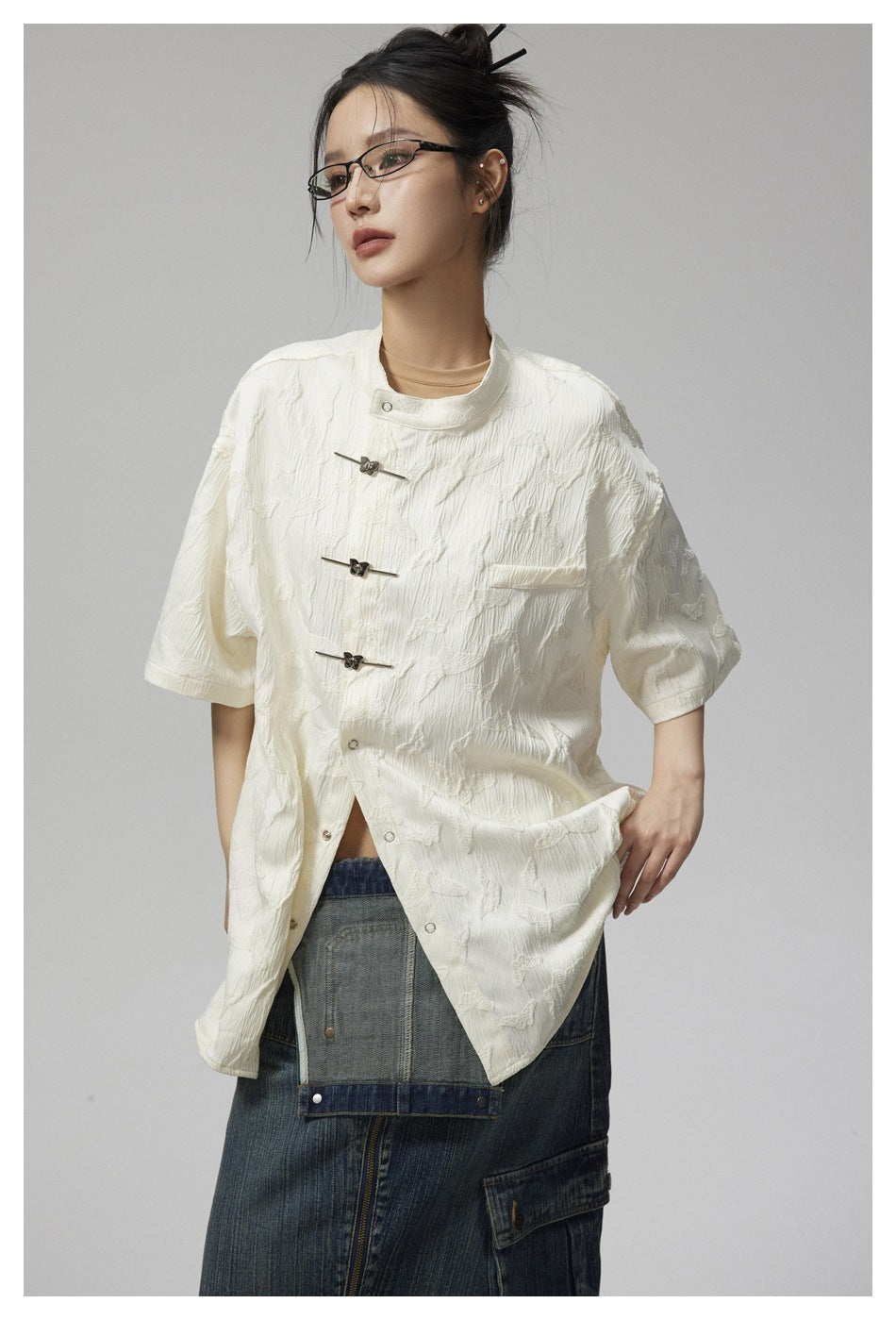 Model wearing an ivory patterned jacket with short sleeves, a stand collar, chest pocket, and frog closures.