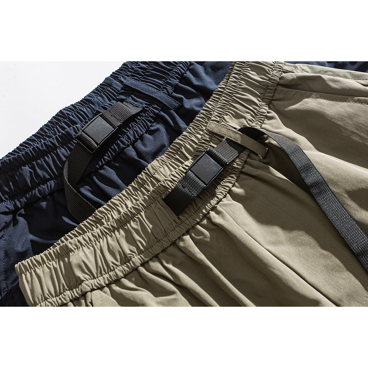 Close-up of khaki and navy shorts showing elastic waistbands and black webbing adjuster straps.