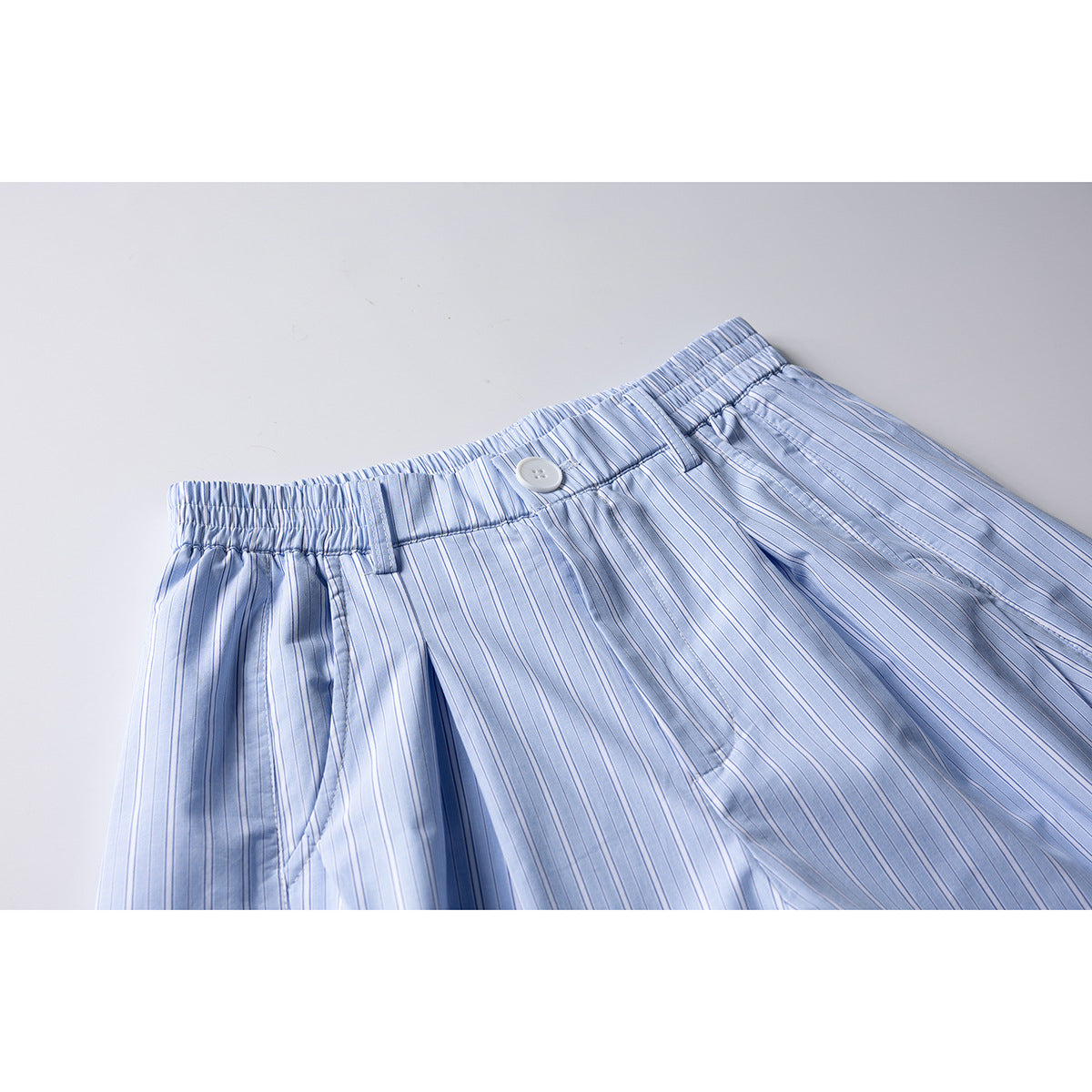 Close-up of light blue pinstriped shorts showing the elastic waistband, white button, belt loops and front pleats.
