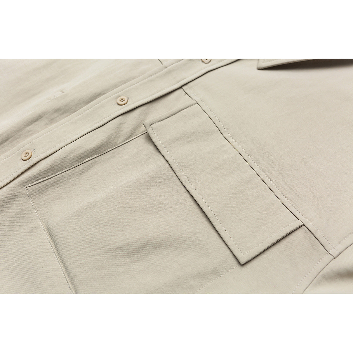 Close-up of a beige shirt's button placket and rectangular chest pocket with visible stitching.