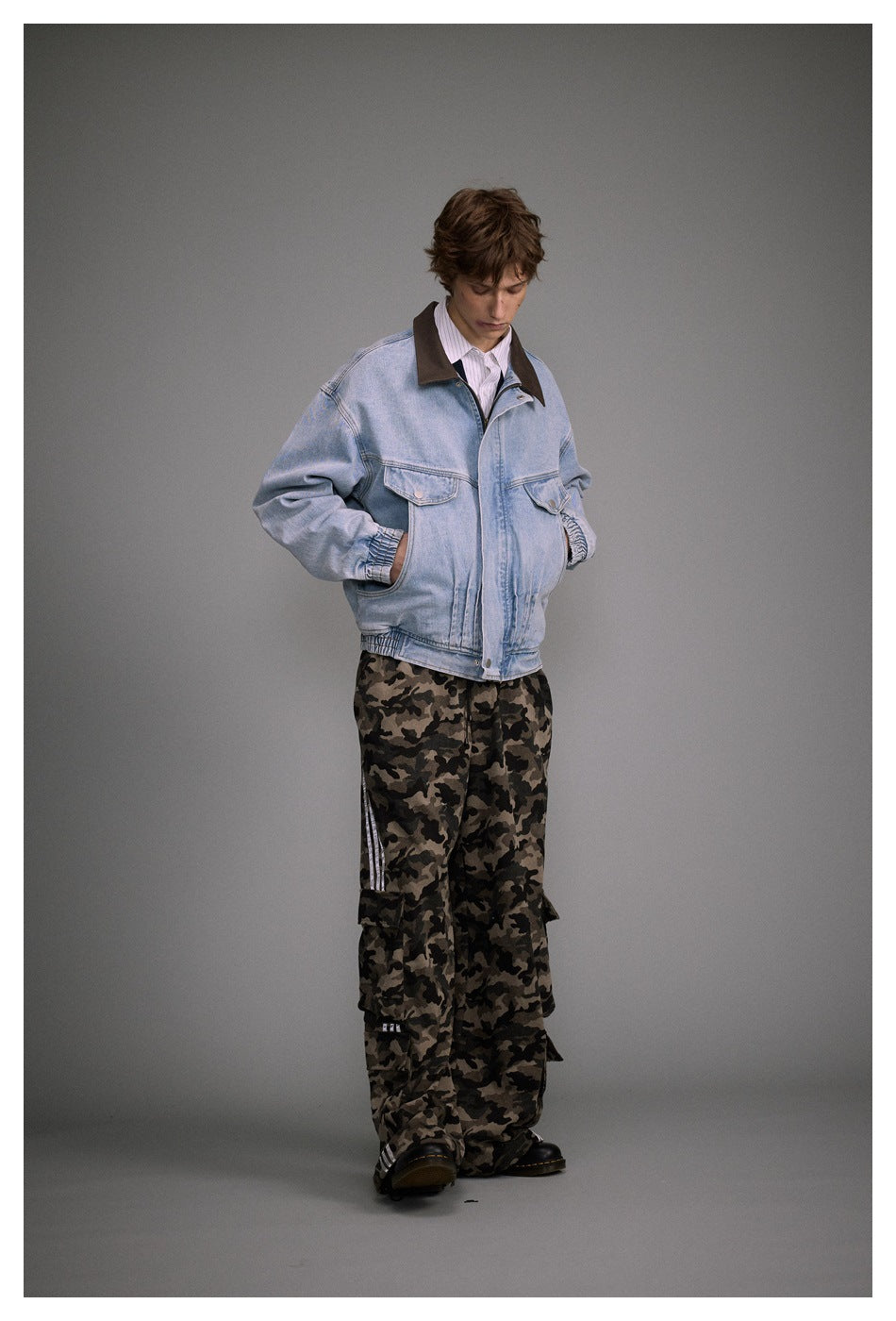 Full-length angled view of a model wearing a light blue denim jacket with a brown collar and camouflage trousers.