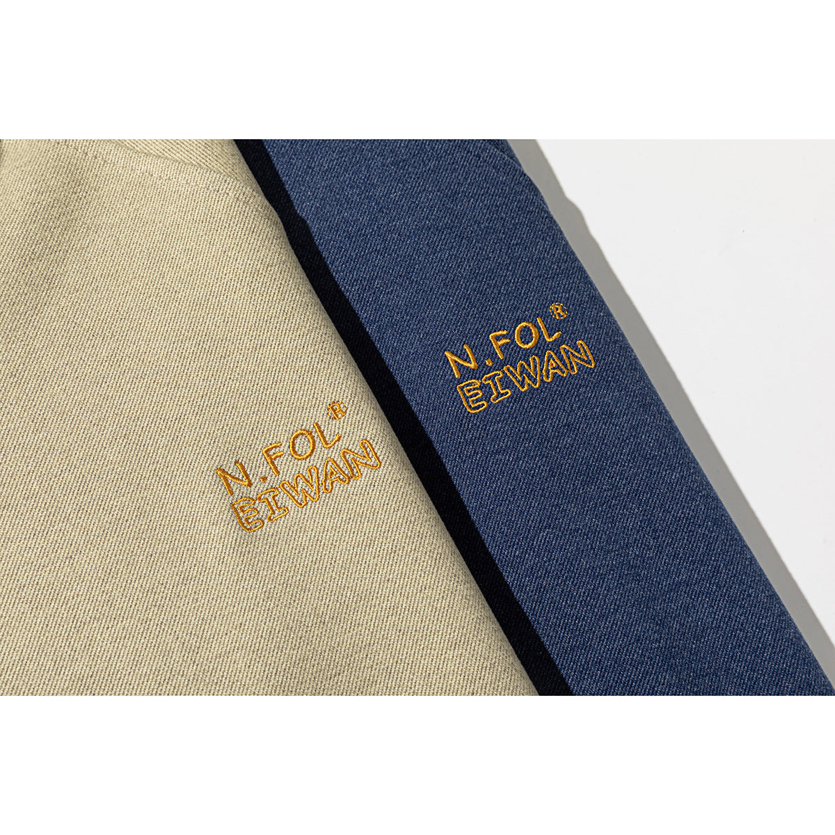 Close-up of beige and navy sweatshirt fabric with small gold embroidered lettering.