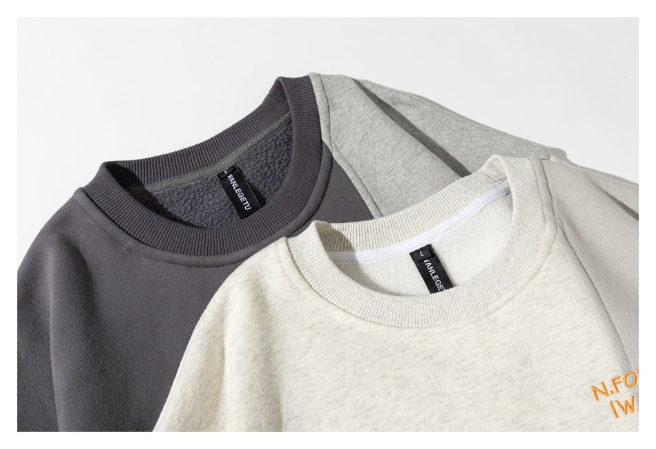 Close-up of two sweatshirts showing ribbed crew necks, inner labels, fleece interiors, and small orange chest lettering.