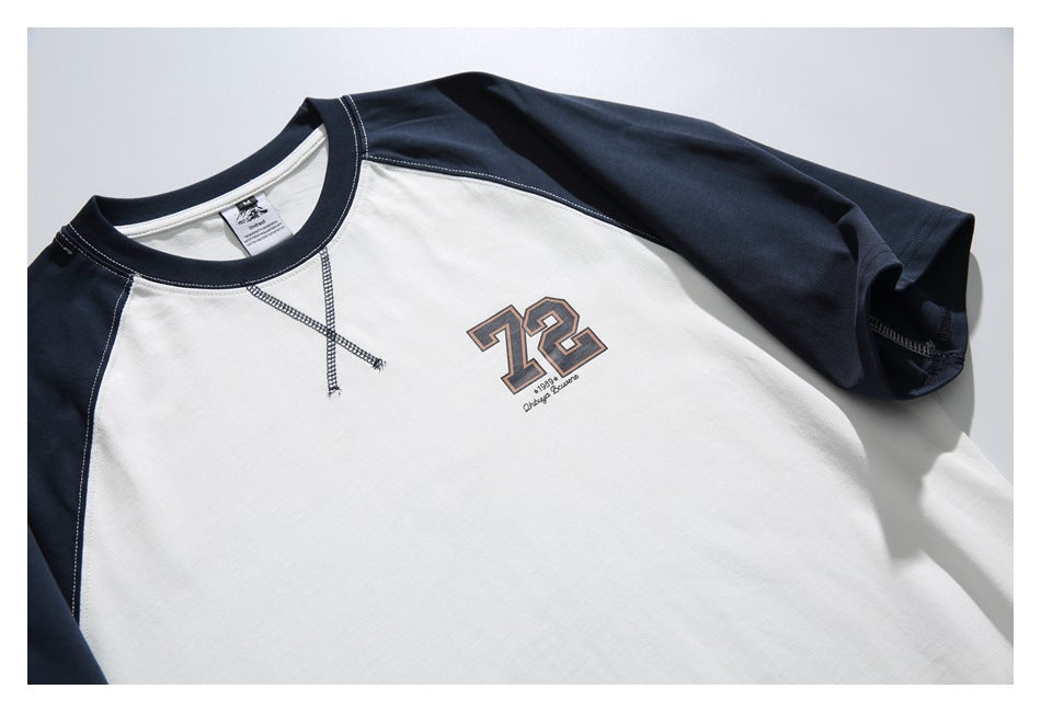 Close view of a white raglan shirt with navy sleeves, contrast stitching, and a small 72 chest graphic.