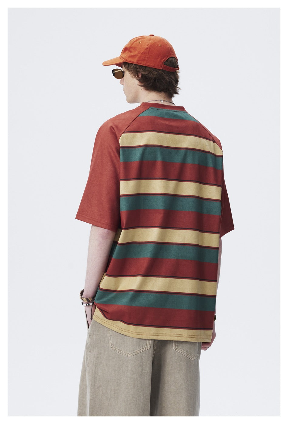 Rear view of a model wearing a rust-red oversized T-shirt with broad teal and cream horizontal stripes.