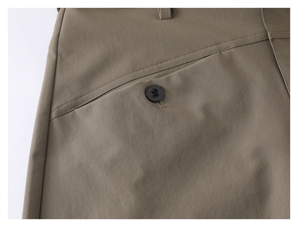 Close-up of a slanted pocket and black button on taupe shorts, with visible stitching.