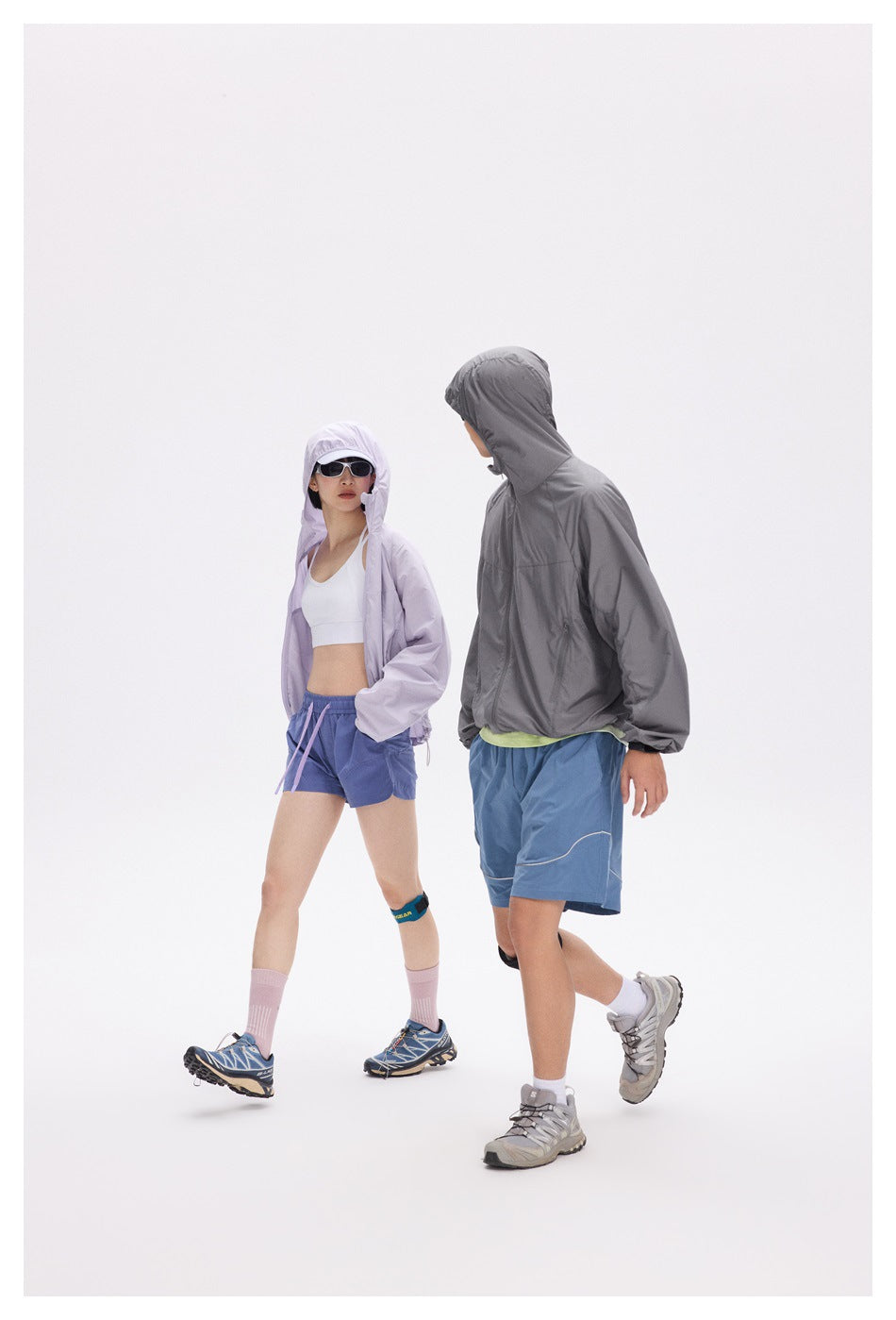 Two models in lavender and charcoal hooded jackets and blue shorts, shown walking in profile.