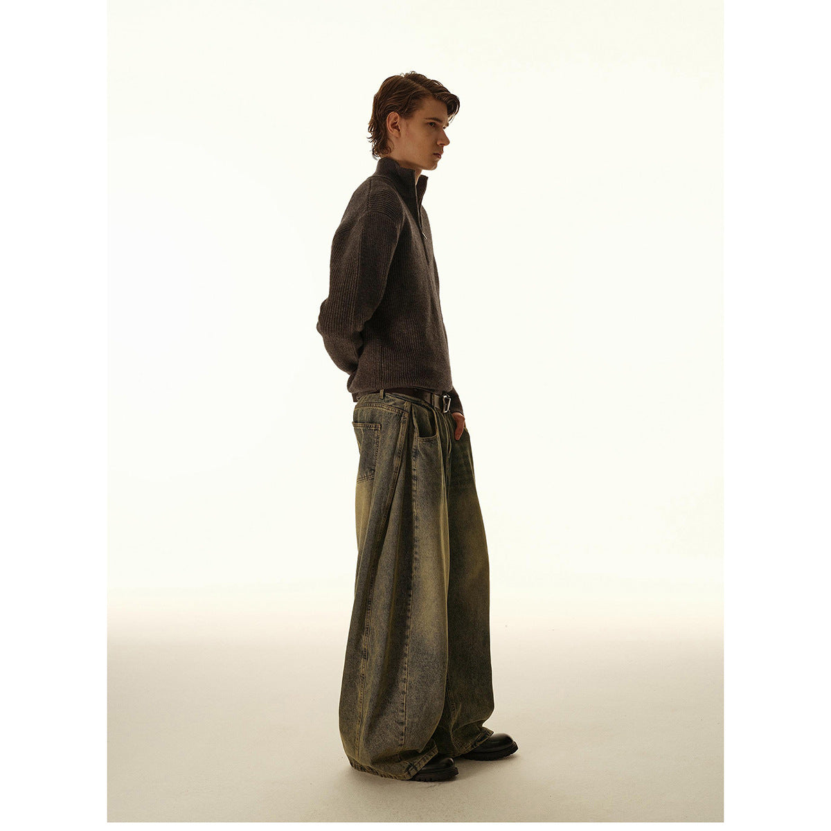 Side view of a model wearing a dark brown high-neck knit pullover and oversized washed jeans.