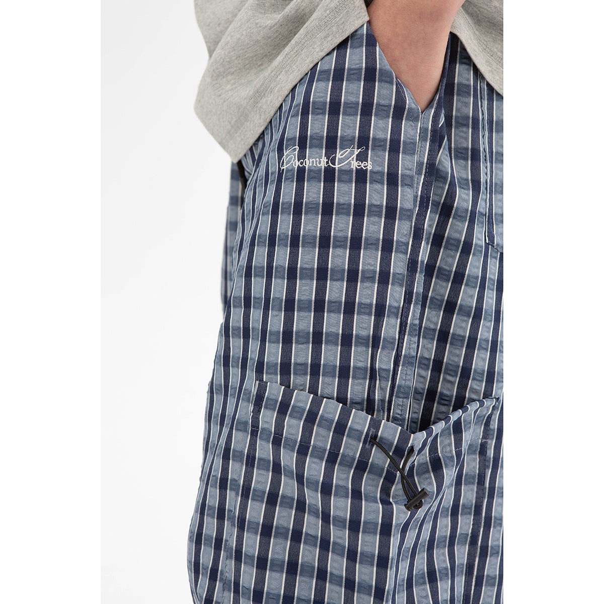 Close-up of blue plaid cargo pants showing embroidered script and a large side pocket with a drawcord.