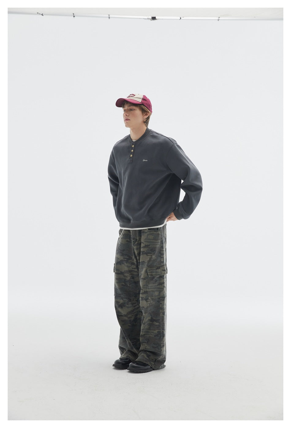 Three-quarter side view of a model in a charcoal henley sweatshirt and loose camouflage cargo pants.