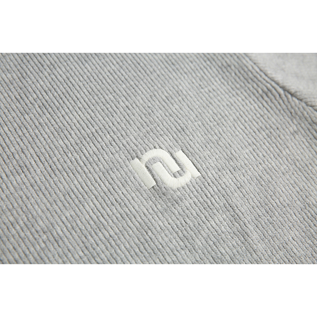 Close-up of a small white embroidered emblem on the light gray ribbed sweater.