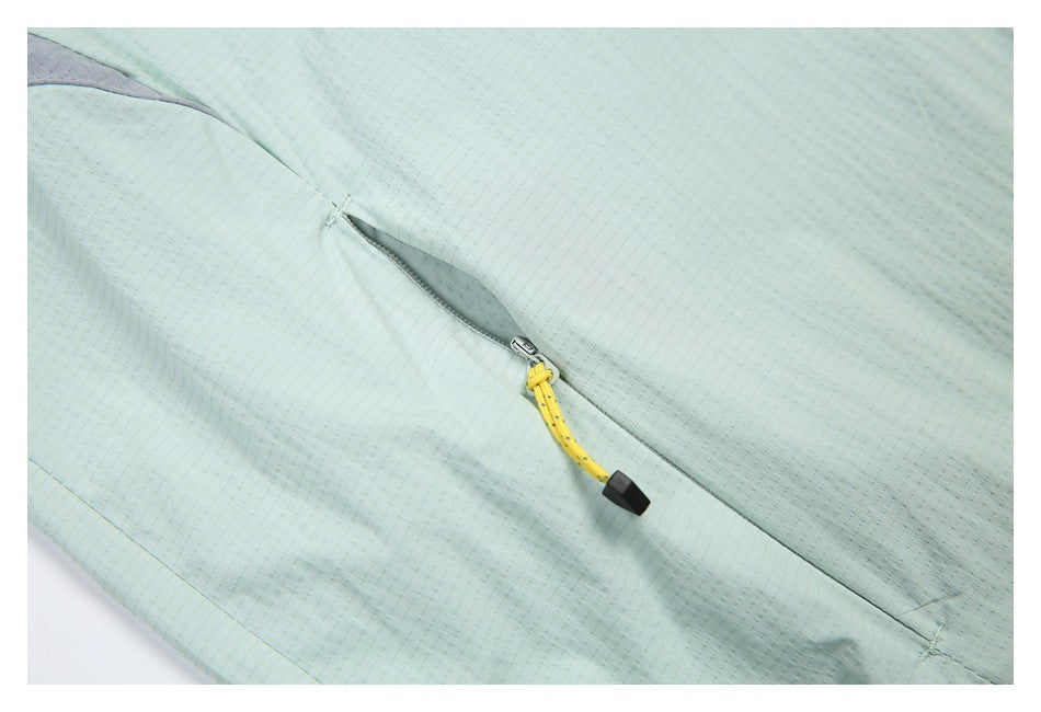 Close-up of a pale mint jacket pocket with a yellow-and-black zipper pull and gray trim.