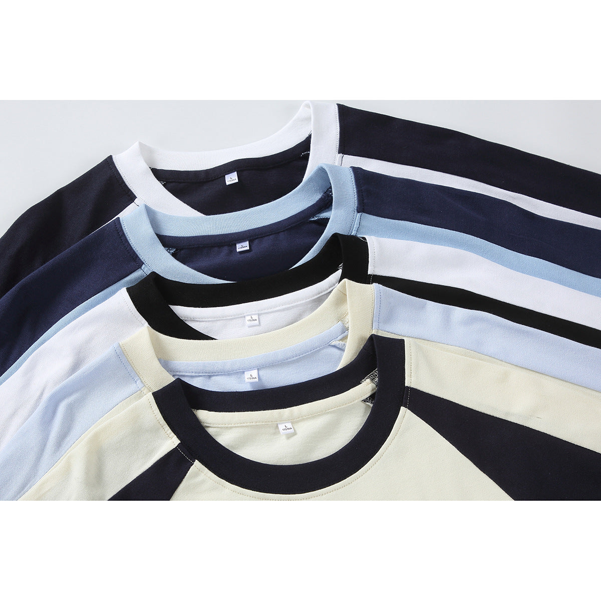 Several overlapping raglan T-shirts in navy, blue, white, and cream, shown from the front.