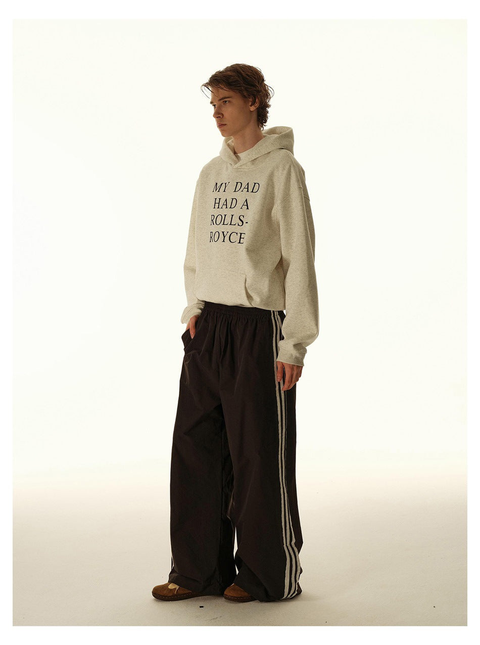 Model wearing a cream graphic hoodie and loose black track pants with light side stripes.