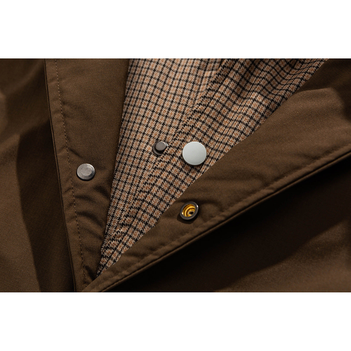Close-up of a brown jacket’s checked lining, metal snaps, and fabric panels.
