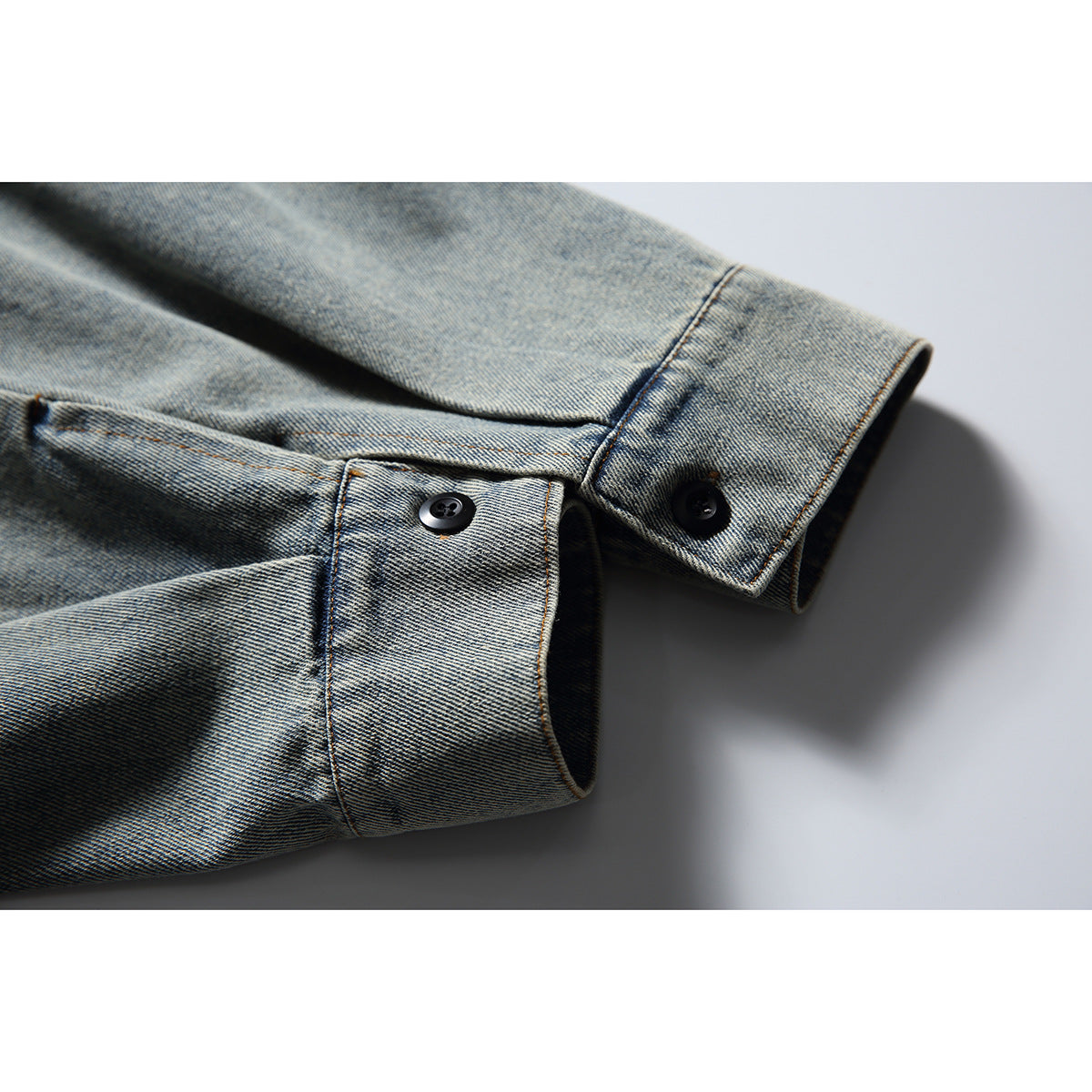 Close-up of the denim jacket's sleeve cuff, showing black buttons and contrast stitching.