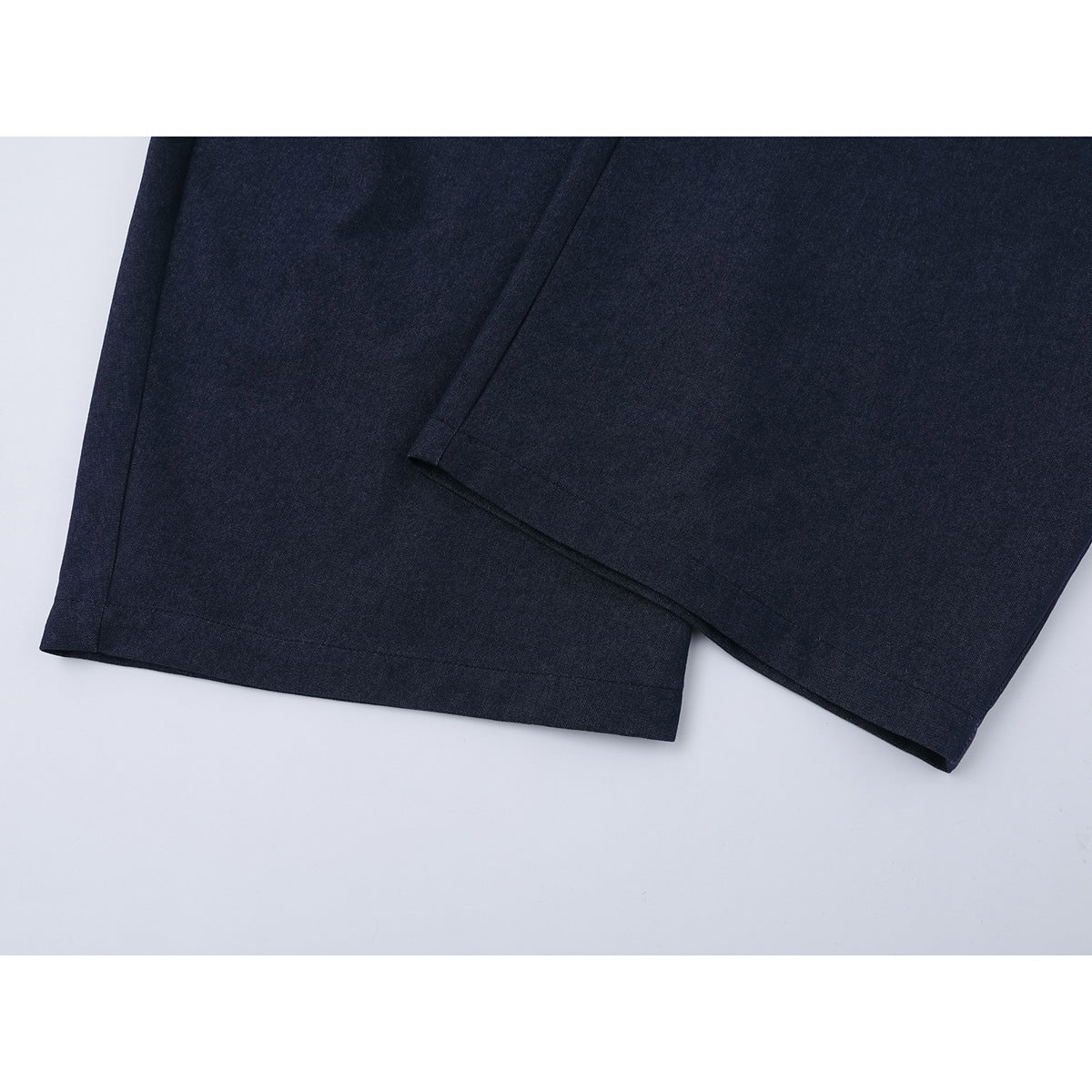 Close-up of the hems of dark navy trousers, showing the straight stitched edges and wide legs.