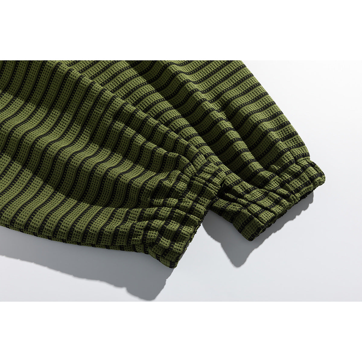 Close-up of the gathered cuff and striped olive-green and black fabric of a long-sleeve top.