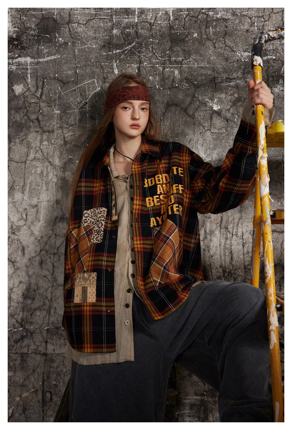 Model wearing a black, red, and mustard plaid patchwork shirt with chest lettering and contrasting patterned pockets.