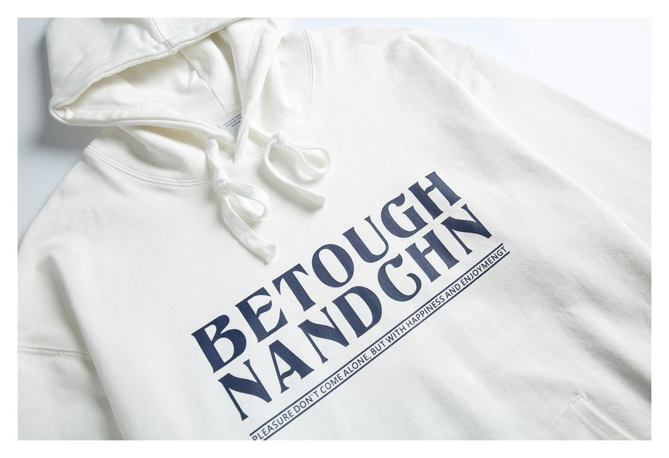 Close-up of a white hoodie showing its hood, drawstrings, and large dark lettering across the chest.