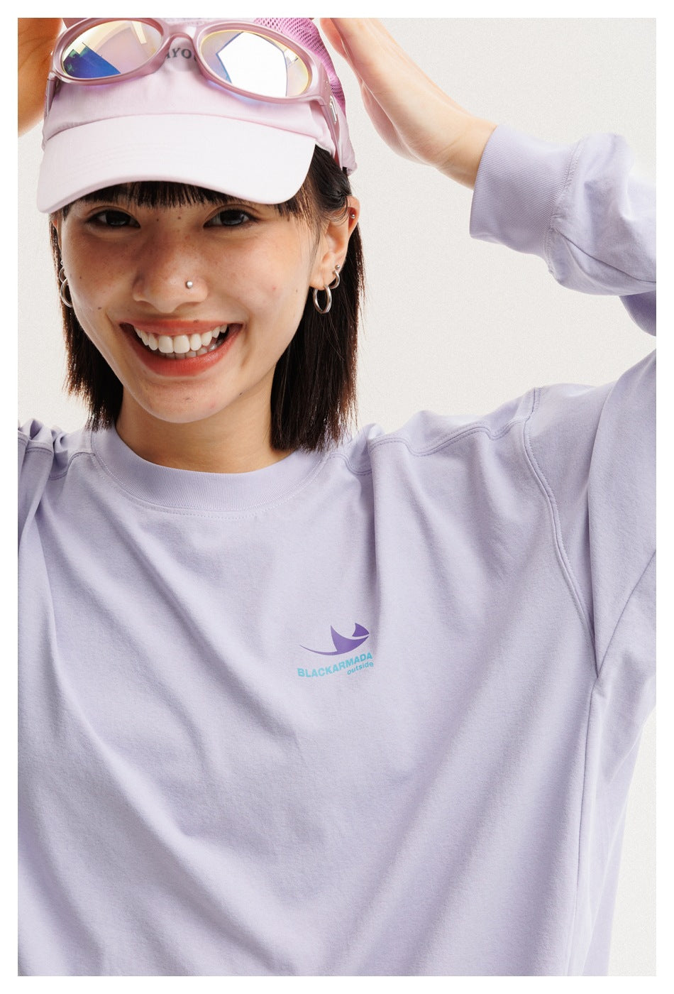 Close-up of a smiling model wearing a lavender sweatshirt with a small chest graphic.