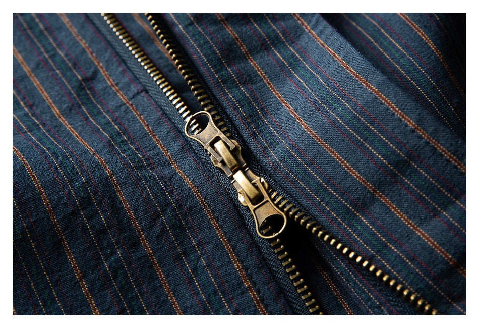 Close-up of a brass two-way zipper on dark blue fabric with thin multicolor stripes.