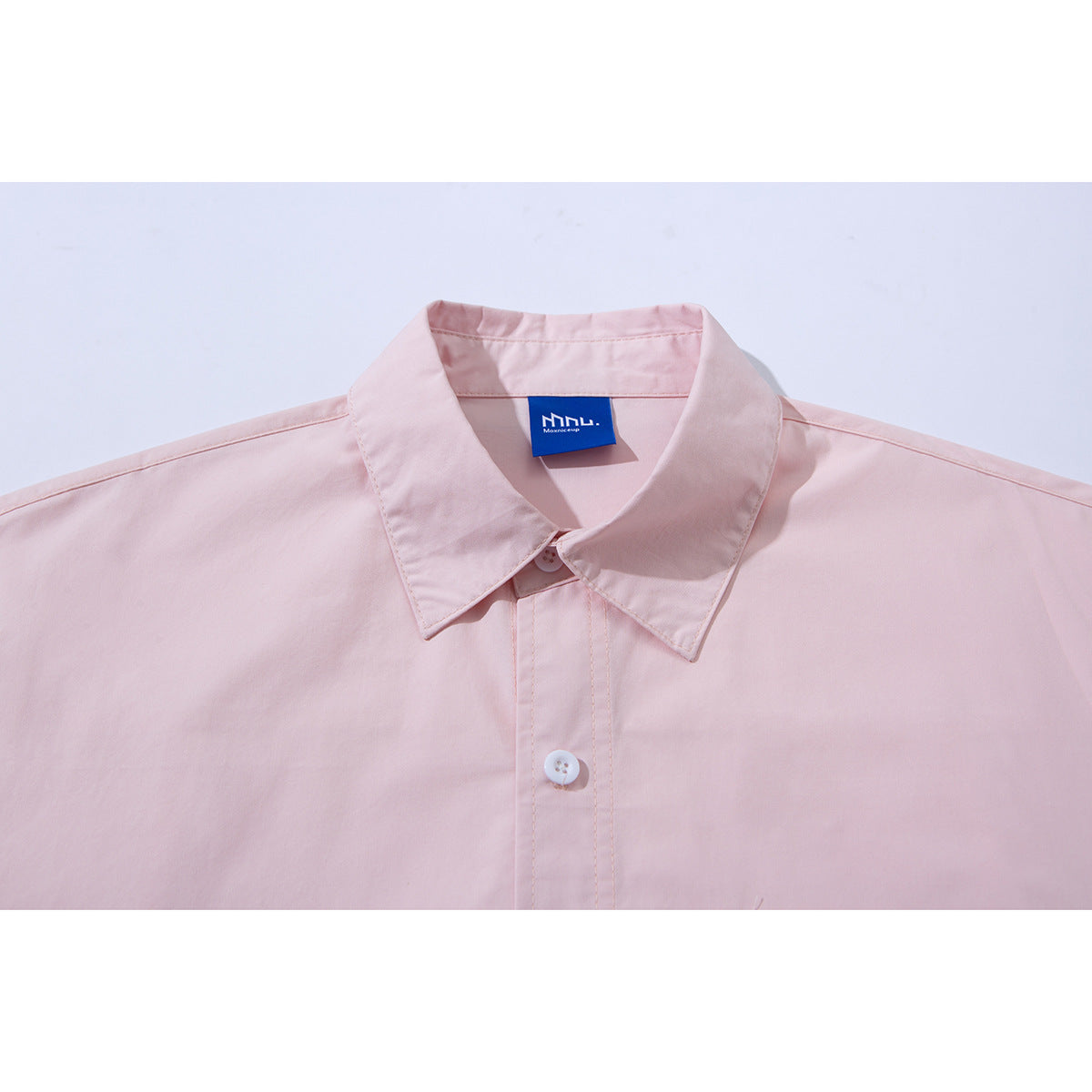 Close-up of a pale pink shirt collar, button placket, and blue neck label.