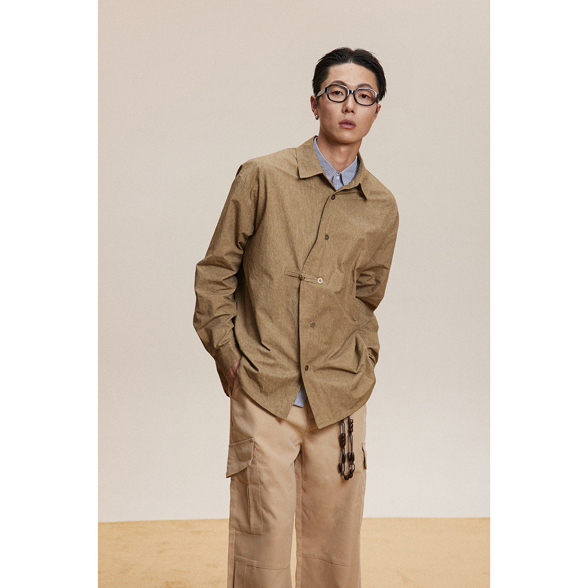 Standing model wearing a brown button-front overshirt over a striped shirt and beige cargo trousers.