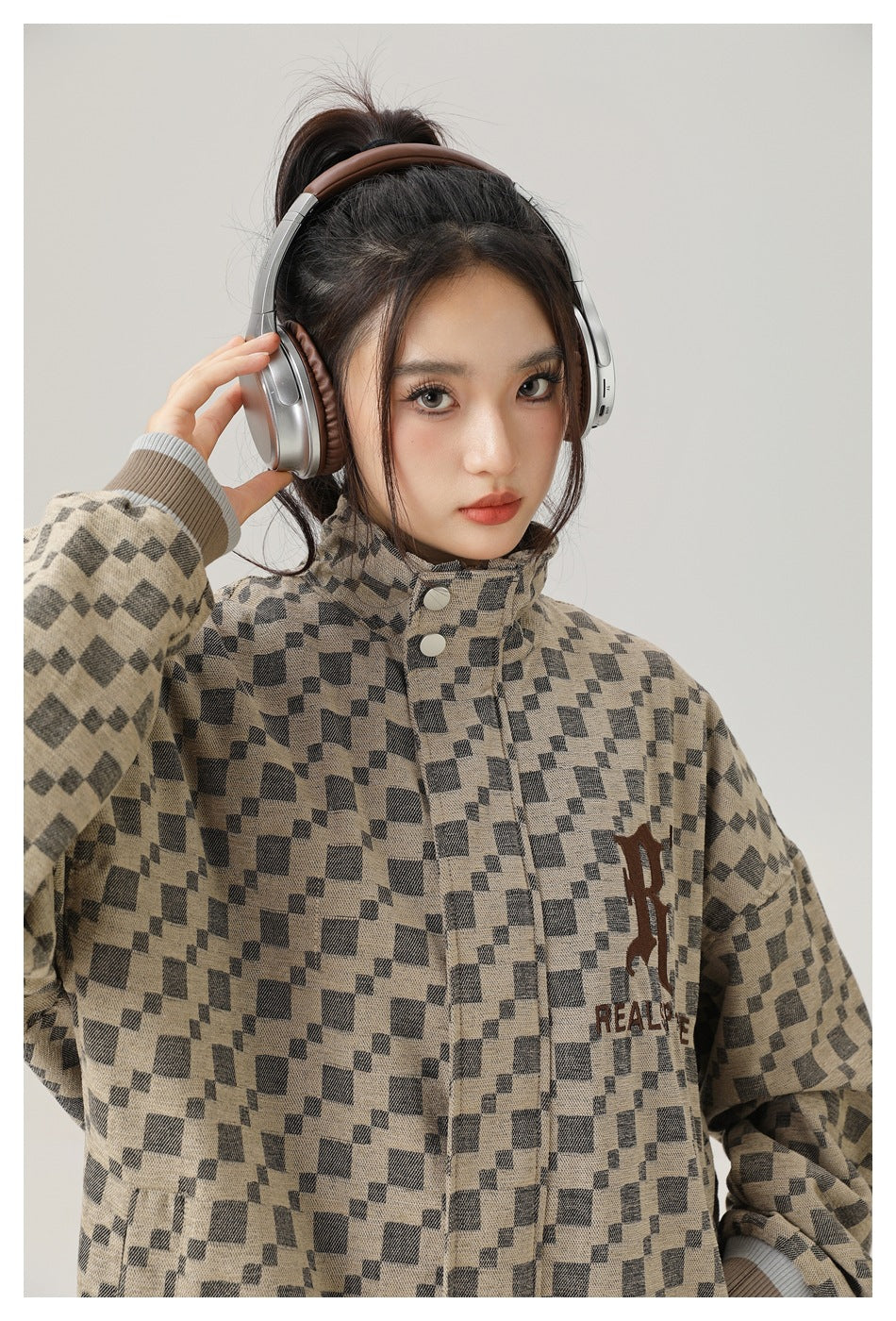 Close-up of a model wearing a beige-and-charcoal checker jacket with a stand collar, snap front, and chest lettering.