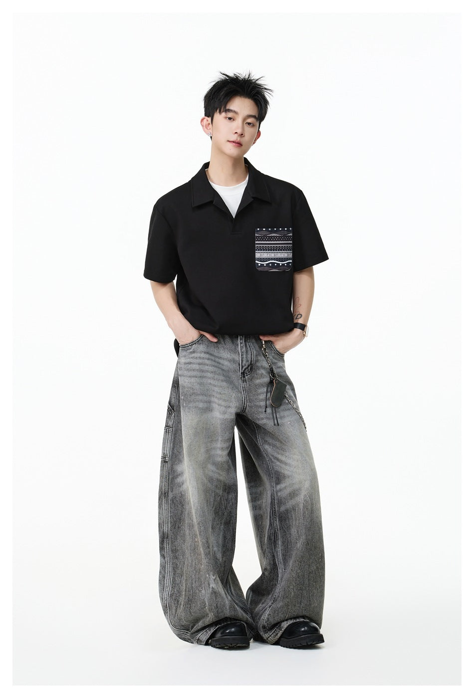 Model standing in a black short-sleeve polo-style top with patterned chest pocket, wide-leg faded gray jeans and black boots