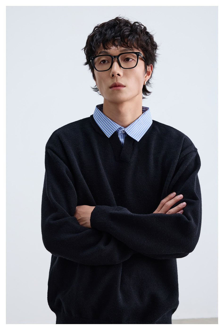 Close view of a model wearing a black V-neck sweater over a blue-and-white striped collared shirt.