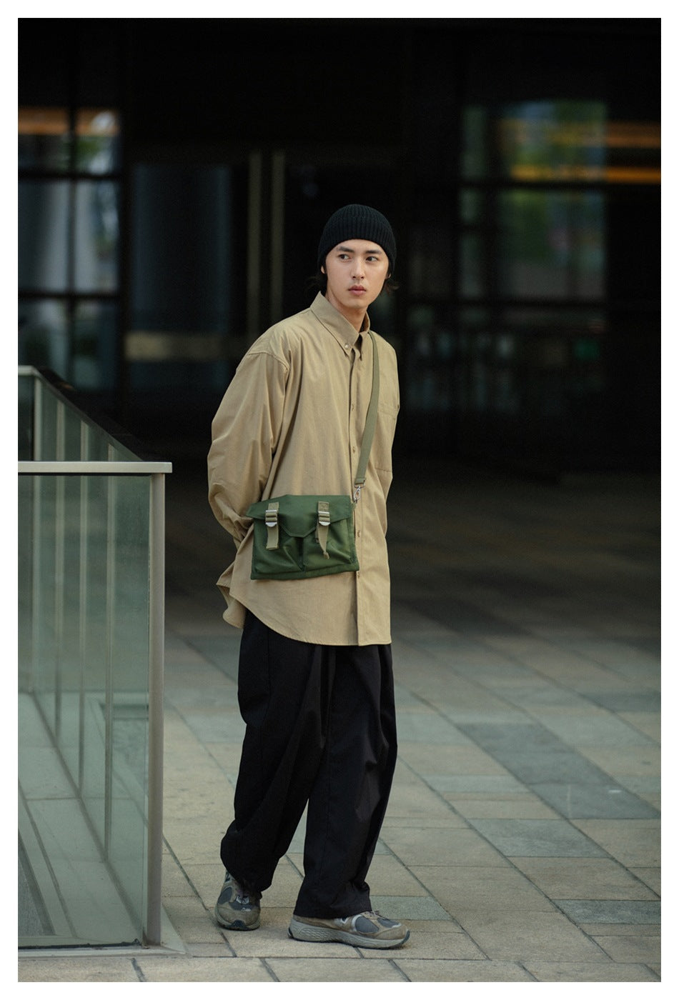 Model wearing an oversized khaki button-up shirt and black trousers, with a green crossbody bag.