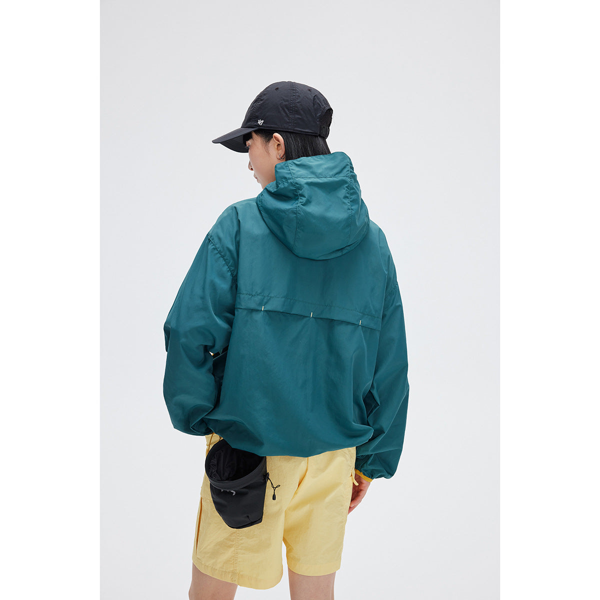 Back view of a model wearing a teal hooded jacket with a horizontal back seam.