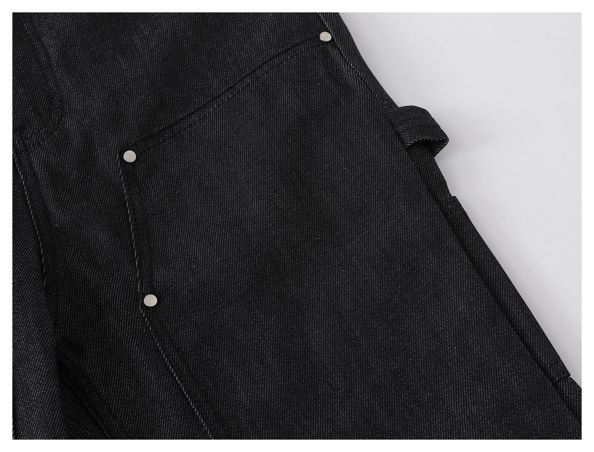 Close-up of black pants showing a large stitched pocket panel with silver rivets.