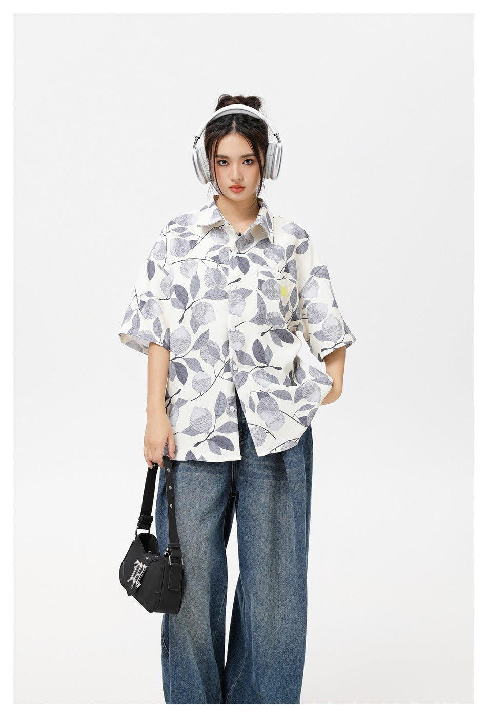 Model wearing an ivory short-sleeve shirt with a gray botanical print, styled with blue jeans, headphones, and a black bag.