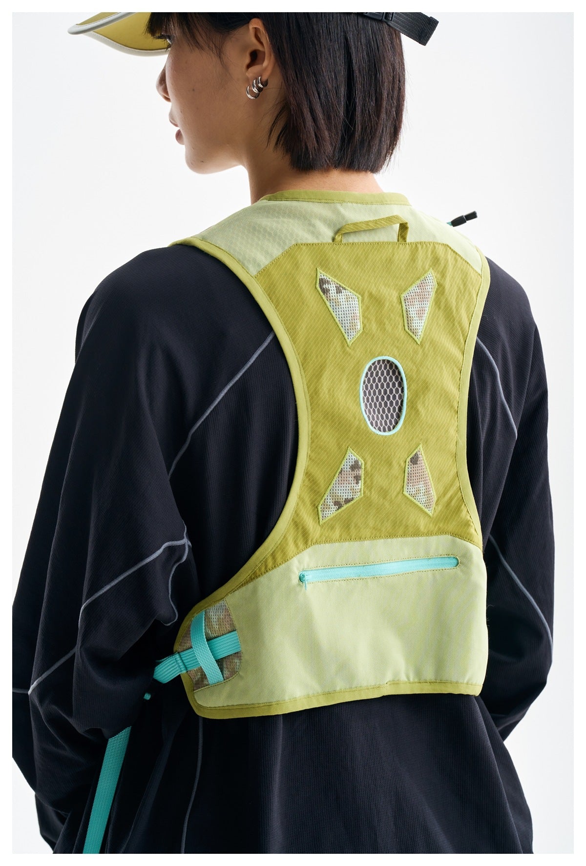 Back view of an olive hiking vest worn over a black top, with mesh panels, turquoise accents and a zip pocket.