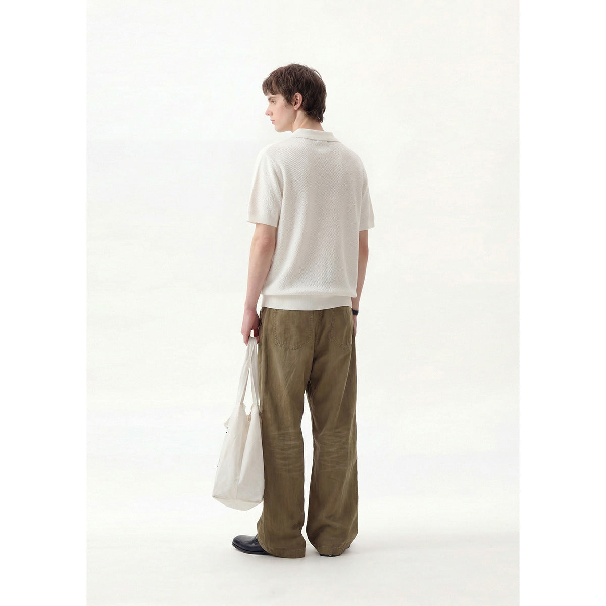 Rear view of a model wearing a white short-sleeve polo with olive-brown trousers.