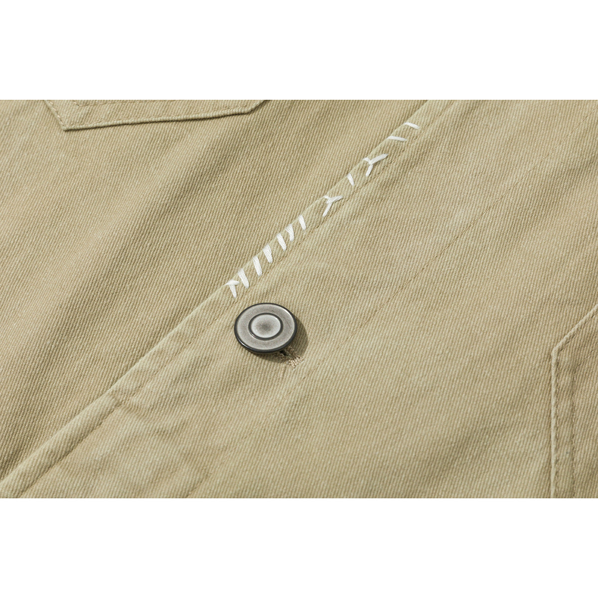 Close-up of tan jacket fabric, a metal button, and white decorative stitching.