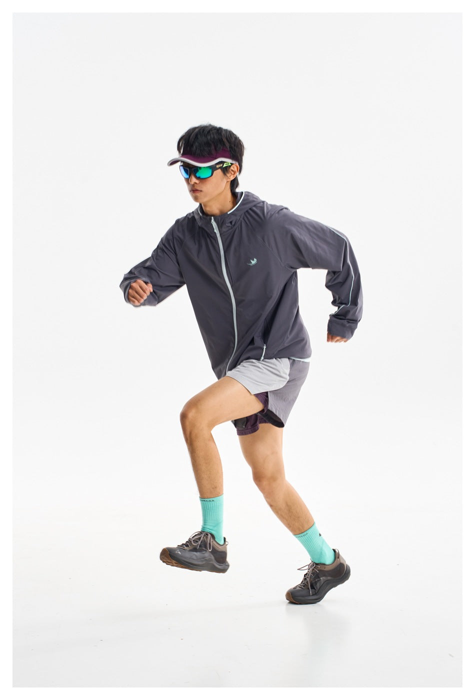 Model running in a charcoal hooded zip jacket with light trim and gray shorts.