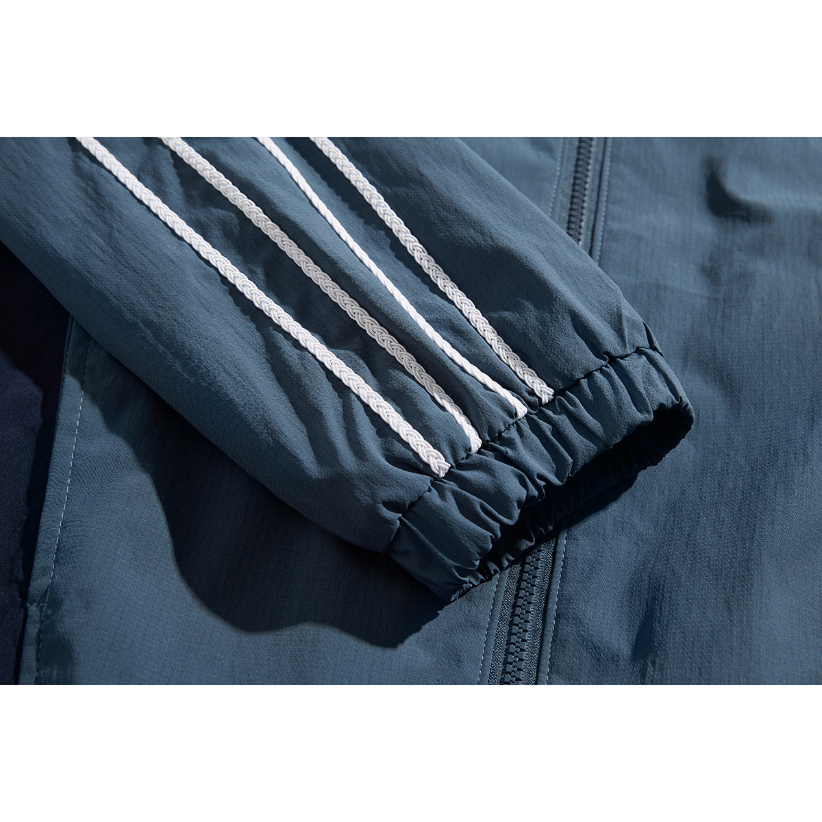 Close-up of a slate-blue jacket sleeve with white braided stripes and an elastic cuff.