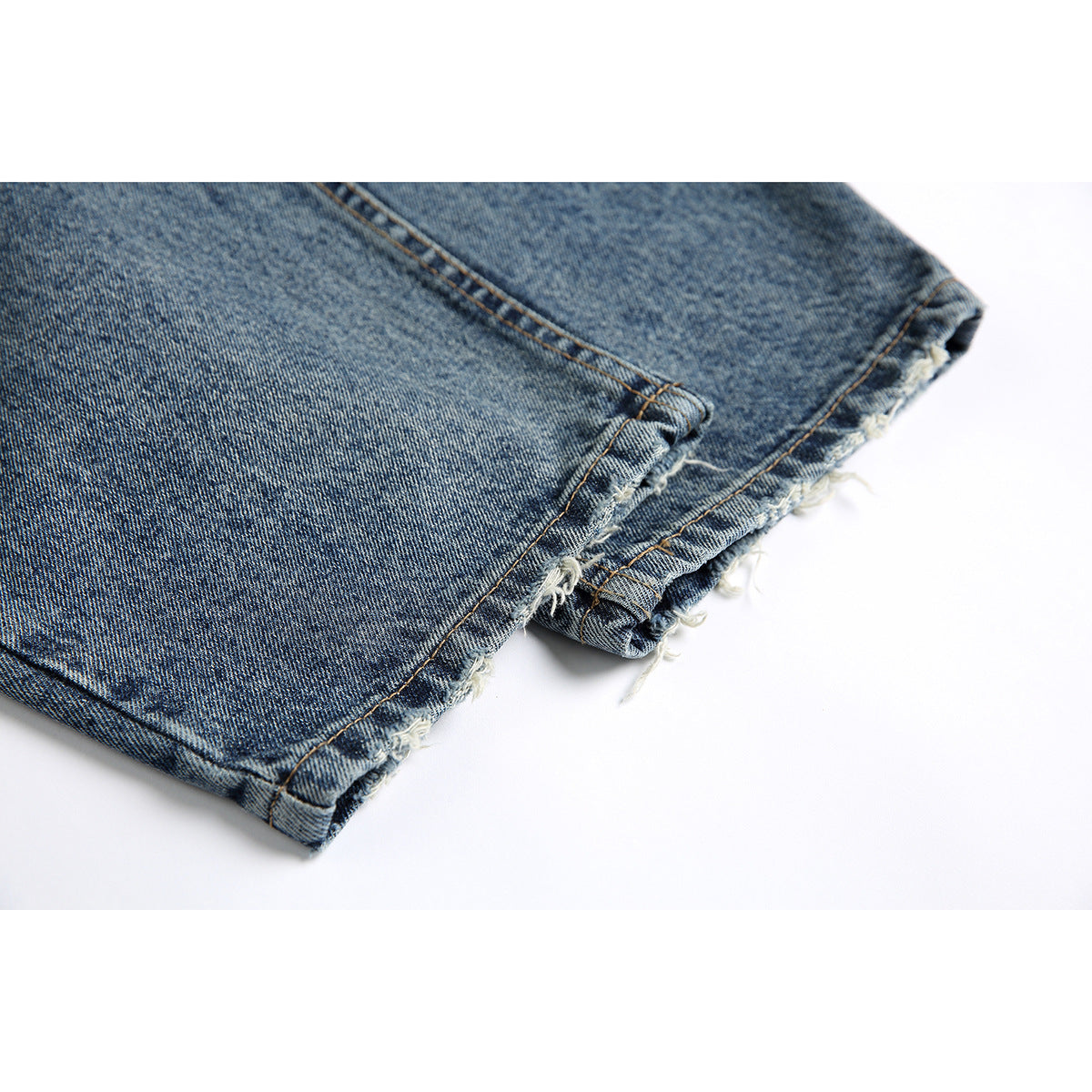 Close-up of the blue denim jeans' cuff with rolled edges and frayed, unfinished hems.