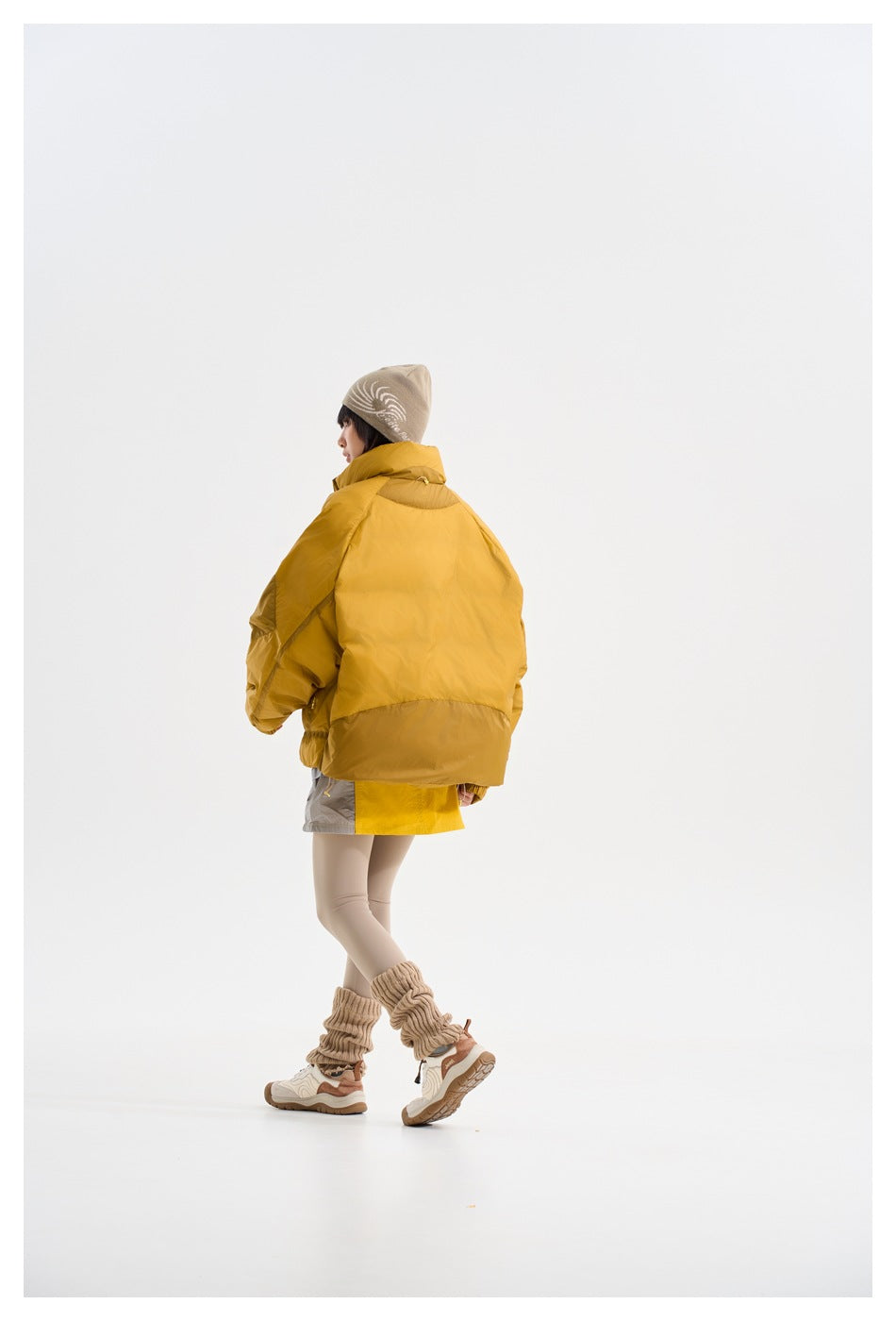 Model wearing a mustard-yellow padded jacket, shown from behind in a walking pose.